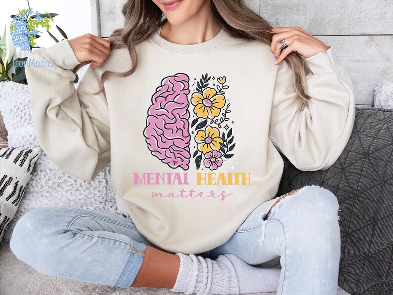 May include: A cream-colored sweatshirt with a pink and white brain graphic and yellow flowers. The text "Mental Health matters" is printed below the graphic.