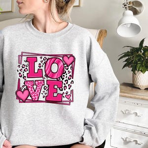 May include: A gray sweatshirt with a pink graphic design that says "LOVE" with leopard print and hearts.