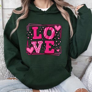 May include: A dark green hoodie with a pink graphic of the word "LOVE" surrounded by hearts and leopard print.