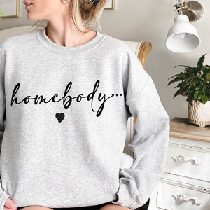 May include: Gray sweatshirt with the text "homebody..." in black cursive lettering and a small black heart.