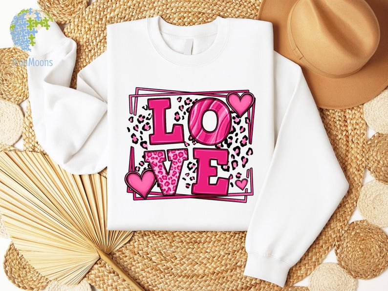 May include: White sweatshirt with a pink "LOVE" graphic. The letters are outlined in black and have a pink leopard print pattern. There are pink hearts around the letters.
