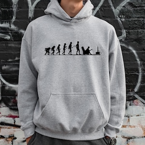 May include: A gray hooded sweatshirt with a black print of the evolution of man, ending with a person sitting in a chair playing a video game.