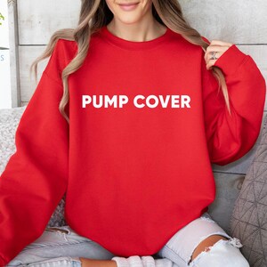 Pode incluir: Um moletom vermelho com o texto "PUMP COVER" em letras brancas. O moletom &eacute; de cor s&oacute;lida e tem mangas compridas. A modelo est&aacute; usando jeans azuis.