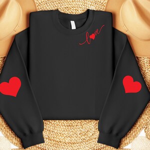 May include: Black sweatshirt with red hearts on the sleeves and the word "Love" with a heart on the front.