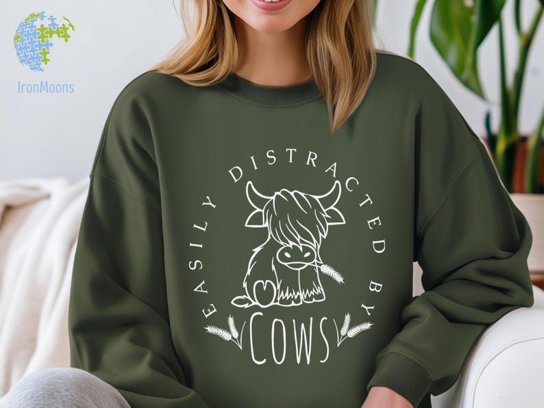 May include: A dark green sweatshirt with a white graphic design. The graphic features a cartoon highland cow with the text "Easily Distracted By Cows".