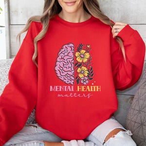 May include: Red sweatshirt with a pink brain and yellow flowers graphic. The text "Mental Health matters" is printed below the graphic.