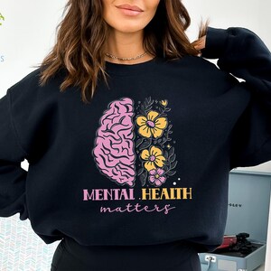 May include: Black sweatshirt with a pink and yellow brain and flowers graphic. The text "Mental Health Matters" is printed below the graphic.