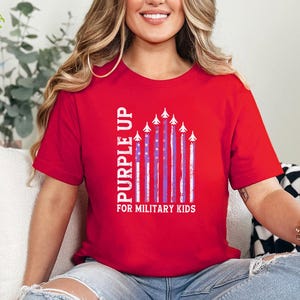 May include: Red t-shirt with the text "Purple Up for Military Kids" and a graphic of purple and white American flags with white airplanes flying in formation.