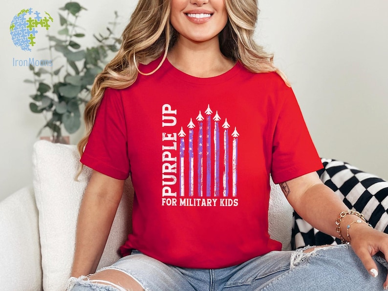 May include: Red t-shirt with the text "Purple Up for Military Kids" and a graphic of purple and white American flags with white airplanes flying in formation.