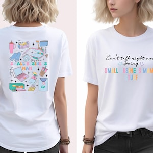 K&ouml;nnte beinhalten: Wei&szlig;es T-Shirt mit einer Grafik verschiedener Kleinunternehmerartikel auf der R&uuml;ckseite und dem Text "Can't talk right now Doing SMALL BUSINESS MAMA STUFF" auf der Vorderseite.