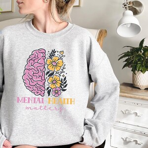 May include: A gray sweatshirt with a pink and yellow brain and flowers graphic. The text "Mental Health matters" is printed below the graphic.