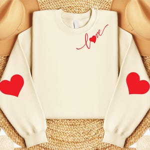 May include: A cream-colored sweatshirt with red hearts on the sleeves and the word "love" with a heart on the front.