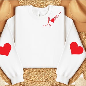 May include: White sweatshirt with red hearts on the sleeves and the word "love" with a heart on the front.