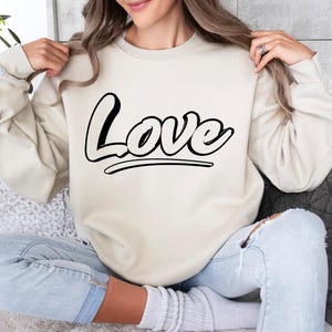 May include: A cream colored sweatshirt with the word "Love" printed in black on the front.