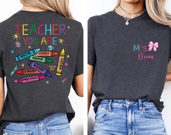 May include: Dark gray t-shirt with the words "Teacher You Are" in colorful letters and crayon graphics. The back of the shirt has the words "Special, Lovely, Unique, Strong, Precious, Blessed, Chosen" on the crayons. The front has "Mrs. Brown" with a bow.