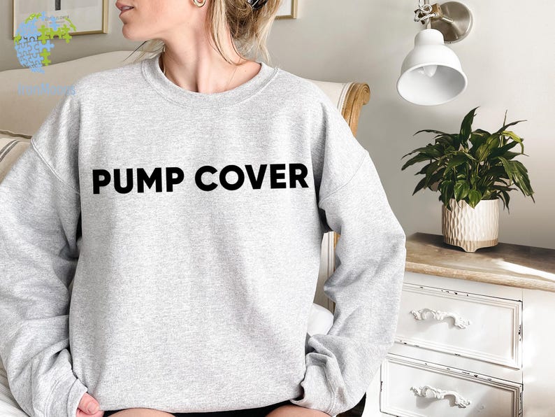 Pode incluir: Um moletom cinza claro com as palavras "PUMP COVER" impressas em letras pretas em negrito no peito. O moletom tem mangas compridas e gola redonda. A imagem mostra uma pessoa usando o moletom.