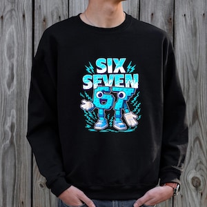 May include: Black sweatshirt with a blue graphic design. The design features the words "SIX SEVEN" in a stylized font, along with animated blue numbers with arms, legs, and shoes. The sweatshirt is made of a soft material.