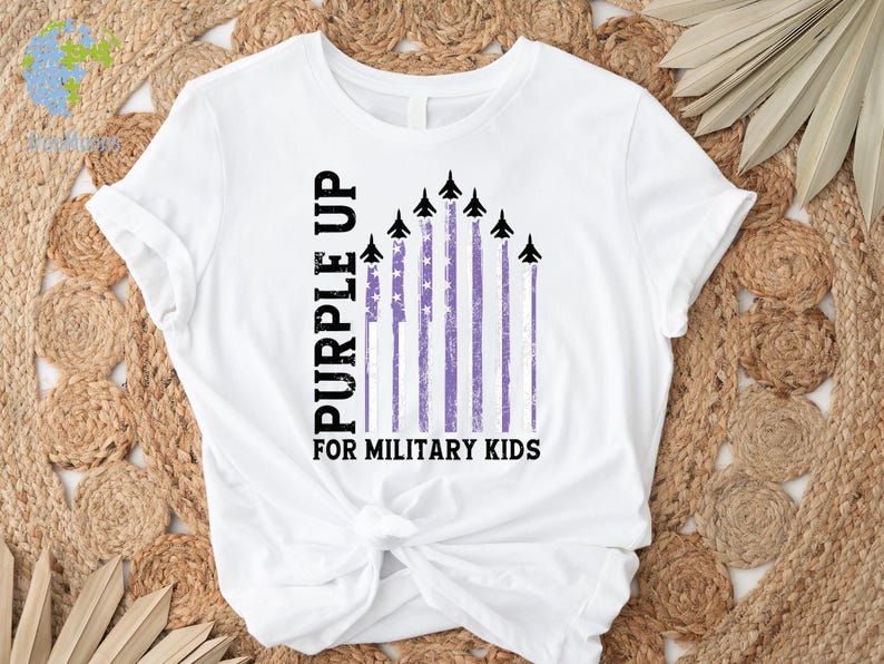 May include: White t-shirt with a purple up for military kids design. The design features a purple and white American flag with black fighter jets flying over it.