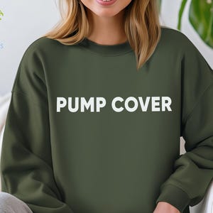 Pode incluir: Camisola verde-oliva com o texto "PUMP COVER" em letras brancas. A camisola &eacute; de cor lisa e tem gola redonda. O log&oacute;tipo IronMoons est&aacute; no canto superior esquerdo.