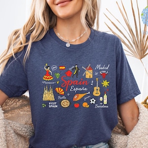 May include: A navy blue t-shirt with a colorful graphic of Spain-related icons, including a flamenco dancer, bull, guitar, and the words "Spain" and "España". The shirt has short sleeves.