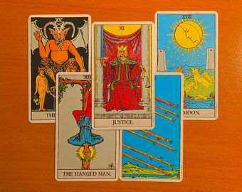 May include: A tarot card spread featuring six cards. The cards include "The Devil," "The Hanged Man," "Justice," "Eight of Wands," and "The Moon." The cards have colorful illustrations and text.