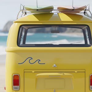 Puede incluir: Una furgoneta amarilla vintage con parachoques blanco y baca con dos tablas de surf. La furgoneta tiene una calcomanía de ola azul y está estacionada en una playa de arena. Las luces traseras de la furgoneta son rojas y naranjas.