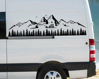 May include: A white van featuring a black vinyl decal on its side panel. The decal depicts a mountain range, a dense forest of pine trees, a winding road, and a small camper van silhouette, with two birds flying above the peaks.