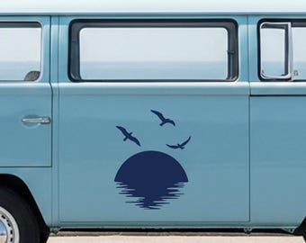 Puede incluir: Una calcomanía azul marino de una puesta de sol sobre el agua con tres pájaros volando. La calcomanía está aplicada en el lateral de una furgoneta azul claro. El sol es un círculo sólido y el agua se representa con líneas horizontales.