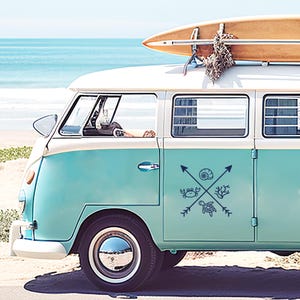 Könnte beinhalten: Ein alter türkisfarbener und weißer Van mit einem Surfbrett auf dem Dach, geparkt an einem Sandstrand mit dem Meer im Hintergrund. Der Van hat ein nautisches Design mit einer Krabbe, einer Schildkröte, einer Muschel und Korallen.