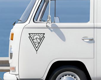 May include: A white van features a black vinyl decal on its side panel. The decal is a triangle containing a sun rising over mountain peaks with radiating sunbeams. Below the triangle are two small dots arranged in a vertical line.