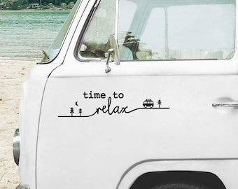 Op de afbeelding: Een witte vintage busje met een zwarte sticker met de tekst "time to relax". De sticker heeft een gestileerd ontwerp van bomen, een halve maan en een camper. De busje staat geparkeerd in de buurt van een strand met uitzicht op de oceaan.