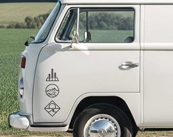 May include: A white van features a black decal on the front side panel. The decal consists of three stacked geometric shapes: a triangle containing pine trees, a circle with mountain peaks, and a diamond enclosing a sun over ocean waves.