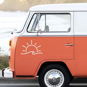 Peut inclure: Un van vintage orange et blanc avec un autocollant blanc représentant un soleil et des vagues sur le côté. Le van a un enjoliveur chromé et une fenêtre. En arrière-plan, une plage floue.