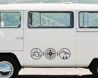May include: A white van featuring a black decal on its side panel. The decal consists of three circular icons arranged horizontally: a sun rising over a wave, a compass rose, and a mountain range with two pine trees, separated by dots.