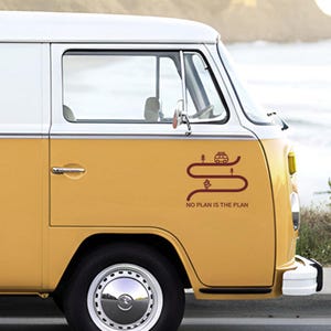 Può includere: Un furgone vintage giallo senape e bianco con una grafica rosso scuro di una strada, alberi e un camper. Il testo "NO PLAN IS THE PLAN" è sotto. Sono visibili lo pneumatico e il coprimozzo del furgone.