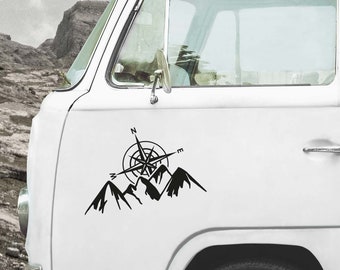 May include: A black vinyl decal applied to the side of a white van, featuring a graphic illustration of a mountain range topped with a compass rose design. The compass includes the cardinal direction letters N, E, and W in a clean, bold font.