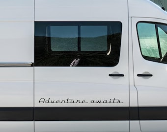 May include: A white van featuring a black vinyl decal on the side panel with the text Adventure awaits in a cursive script font. The vehicle has a sliding door, a rectangular window, and black door handles, with a dark trim strip below.