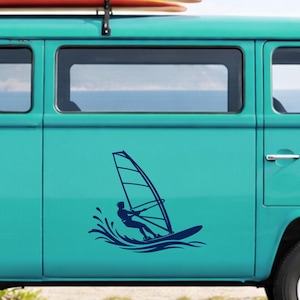 Könnte beinhalten: Ein dunkelblauer Vinyl-Aufkleber mit der Silhouette einer Person beim Windsurfen auf einem Brett mit Segel, dargestellt mit stilisierten Wasserspritzern darunter, angebracht an der Seitenwand eines hellen türkisfarbenen Vans.