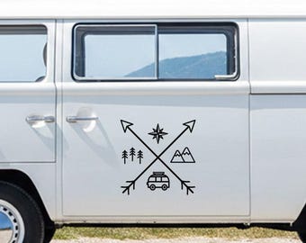 Puede incluir: Gráfico negro de una rosa de los vientos con flechas, árboles, montañas y una furgoneta camper. El diseño está en el lateral de una furgoneta blanca, lo que sugiere un tema de viaje o aventura.