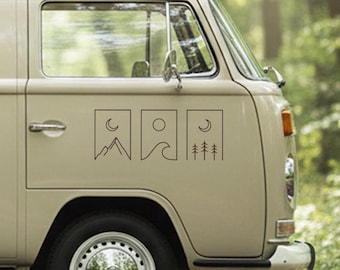 May include: Tan van with three black line art decals. The decals depict a mountain and crescent moon, a sun and waves, and a crescent moon and trees. The van has a chrome hubcap and a front orange marker light.