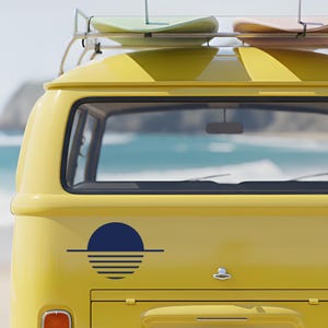 Könnte beinhalten: Ein gelber Oldtimer-Van mit Surfbrettern auf dem Dach, geparkt am Strand. Der Van hat eine blau-weiße Grafik eines Sonnenuntergangs. Die Surfbretter sind in Pastelltönen gehalten.