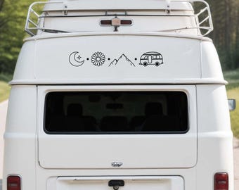 May include: A white camper van featuring a black line art decal on the rear door. The decal displays a sequence of icons including a crescent moon with a star, a daisy flower, a mountain range, and a vintage camper van, separated by small dots.