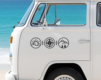 May include: White van with three black circular decals. The decals feature a sunrise over waves, a compass, and a mountain scene with trees. The van is parked near a body of water.