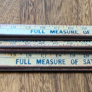 May include: A vintage wooden folding ruler with a yellowed finish and brown metal accents. The ruler is marked with inches from 1/3 to 22 and has the text "FULL MEASURE OF SATISFACTION" printed on it.