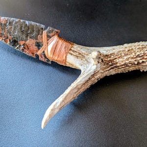 May include: A white ceramic mug with a black handle and the text "But First, Coffee" in a bold, black font. The mug is set against a blurred background, suggesting a cosy setting.