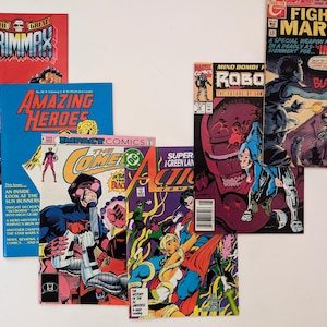 May include: A collection of comic books featuring various characters and titles, including "The Great Grimmax", "Amazing Heroes", "Impact Comics: The Comels", "Super Action: Green Lantern", "Mind Bomb! Robo", and "Fightin' Marines".