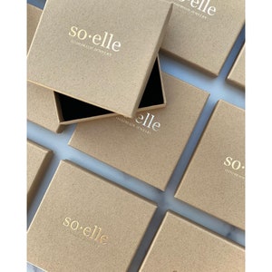 Puede incluir: Varias cajas de cart&oacute;n marr&oacute;n con el texto "so-elle HANDMADE JEWELRY" impreso en dorado en la parte superior de cada caja.