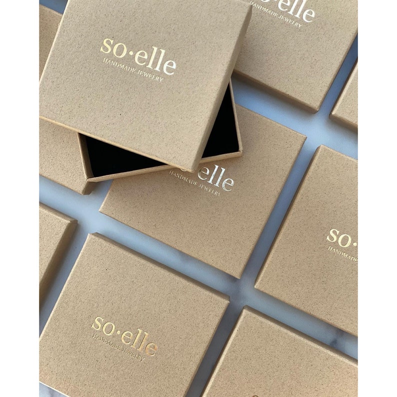 Puede incluir: Varias cajas de cart&oacute;n marr&oacute;n con el texto "so-elle HANDMADE JEWELRY" impreso en dorado en la parte superior de cada caja.