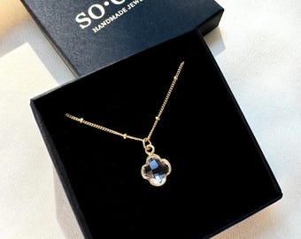 May include: A gold necklace with a clear crystal four-leaf clover pendant. The necklace is in a black box with the text "so.elle HANDMADE JEWELRY".