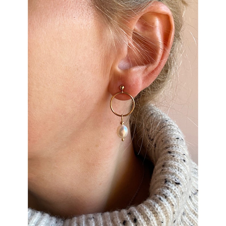 May include: Gold hoop earrings with a single white pearl dangling from the bottom.